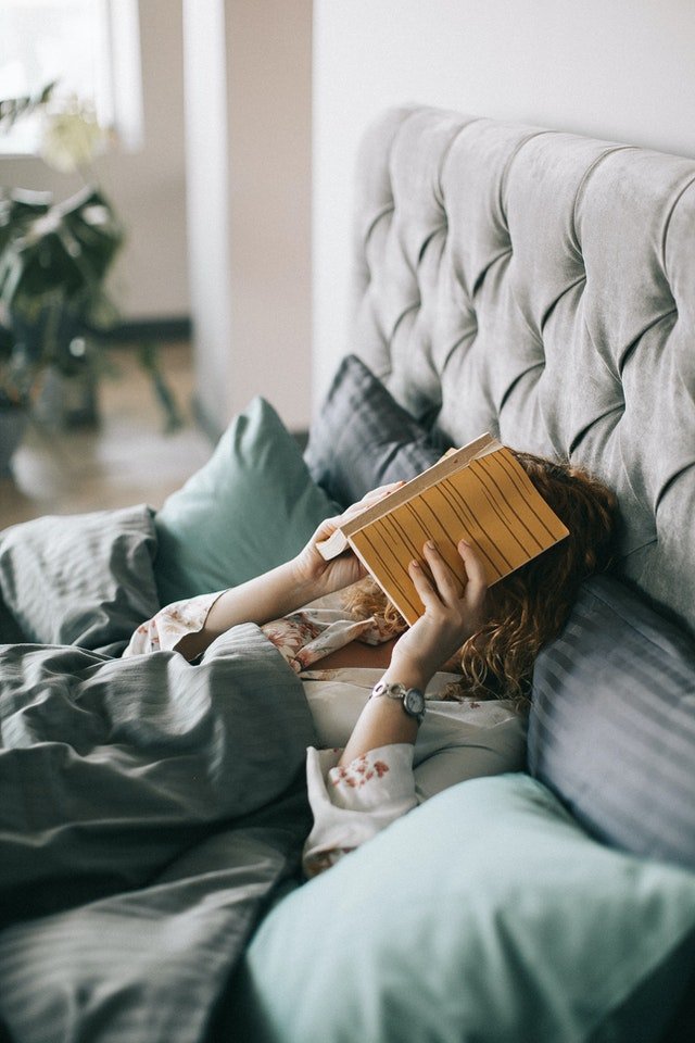 woman covering face with book on bed 1524232 2