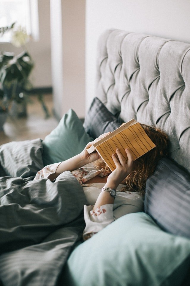 woman covering face with book on bed 1524232
